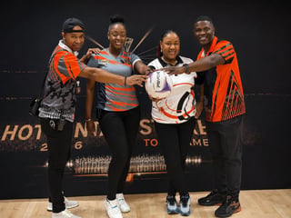 Four people in colorful orange and patterned clothing join hands together in celebration against a dark stage backdrop