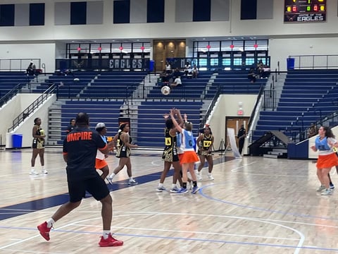 Basketball players during practice in an indoor arena with blue bleachers and EAGLES signage on the scoreboard