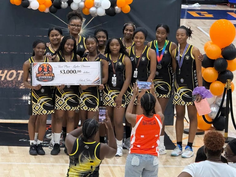 Basketball team holds a $3,000 prize check while wearing gold and black uniforms with medals at tournament celebration
