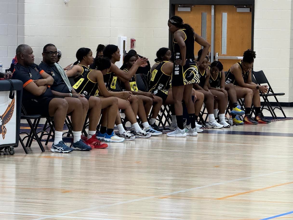 Basketball team sitting together on chairs in a huddle during a timeout or team gathering in an indoor gymnasium.
