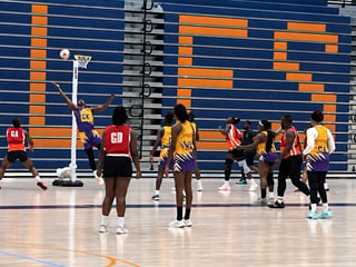 Netball players in yellow and red uniforms practice on an indoor court with blue and orange striped walls during training