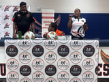 Panel of three people at table with Strikers branded backdrop at indoor community event, reggae music visible on signage