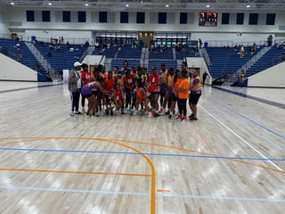 Youth sports team in red and yellow jerseys posing together on indoor gymnasium court with bleachers in background