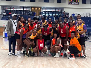 Netball team posing together on court, wearing red and yellow uniforms, with coach on left side