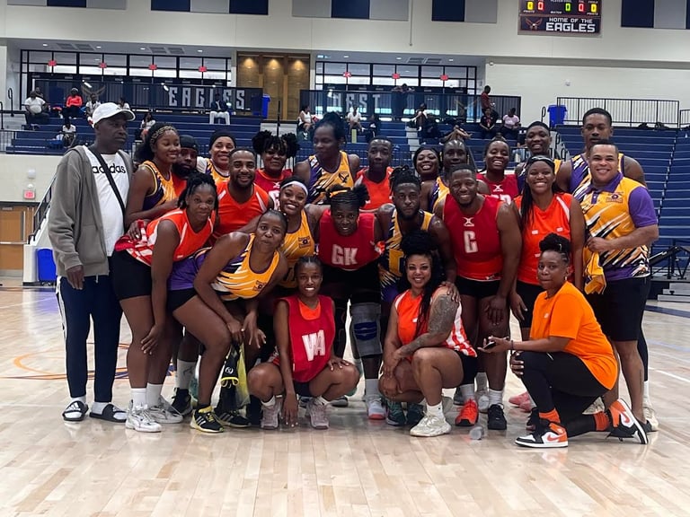 Netball team posing together on court, wearing red and yellow uniforms, with coach on left side
