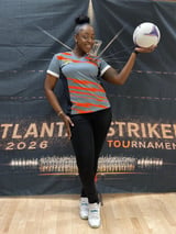 Young female soccer player in orange and gray jersey holding a soccer ball in front of Atlanta Strikers 2026 tournament banner